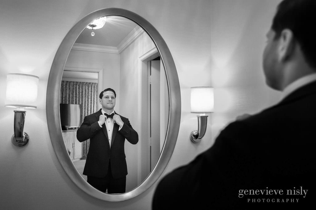 Groom adjusting his bow time in a mirror.