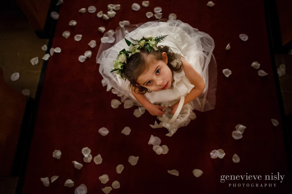 Flower girls looks up while playing with flower pedals during the wedding ceremony.