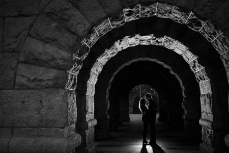 A black and white image of an engaged couple facing each other and standing under an arched stone tunnel in Lincoln Park.