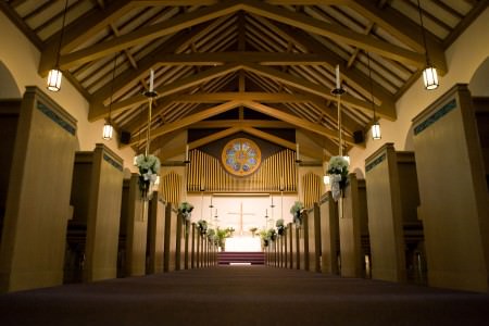 A ground floor view looking down the main aisle towards the altar of The Memorial Chapel in Akron, Ohio with the outside pews decorated with white and green flowers and the stunning wooden beams in the ceiling.