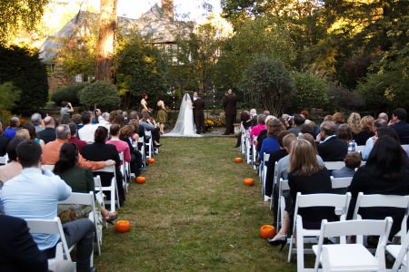An autumn wedding ceremony in the backyard of the O'Neil House in Akron, Ohio with pumpkins lining the grass aisle leading to the altar with the tudor style home in the background with trees.