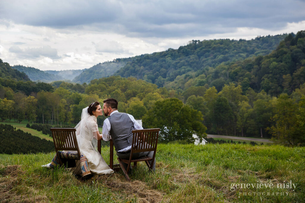 Bride and groom sit at a table overlooking a valley on their wedding at Running River Farm near mohican state park in Ohio.