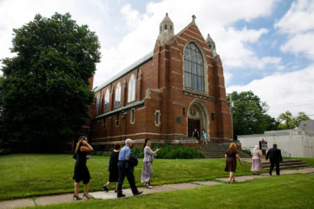 An image of the outside of the Concordia Lutheran Church where a handful of wedding guests are walking on the sidewalk leading up to the brick building.
