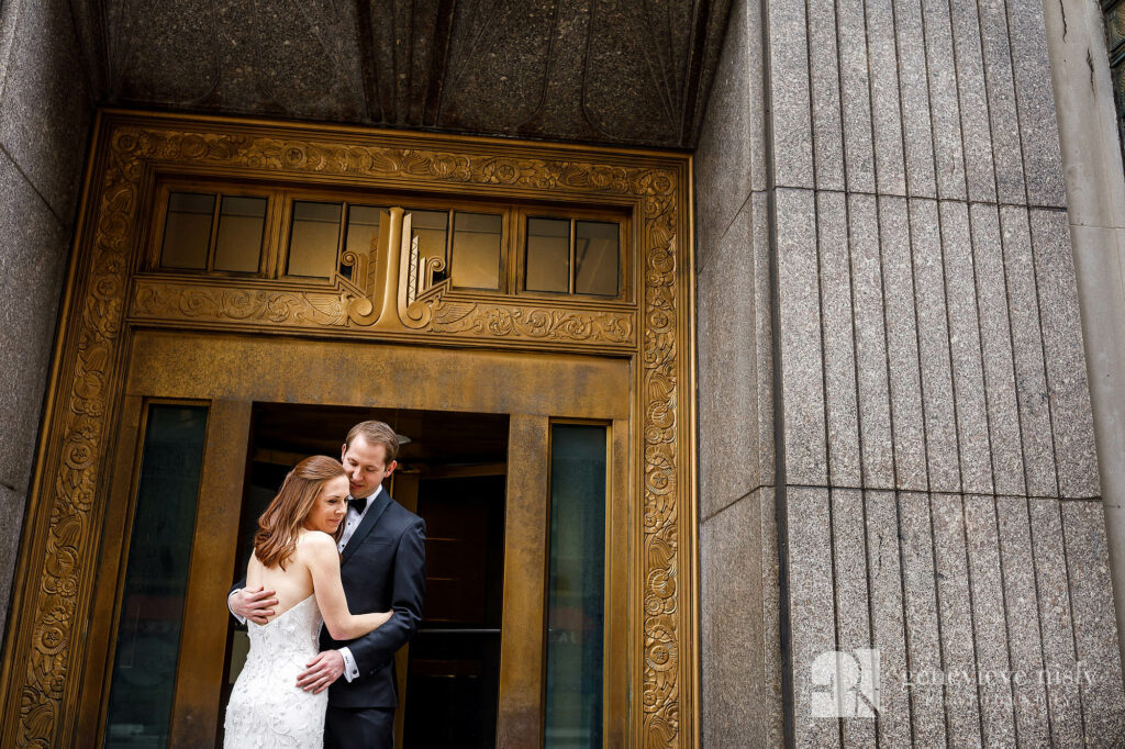Max and Emily in front of a historic gold door in downtown Cleveland during their winter wedding at the Cleveland Museum of Art.